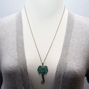 May include: A gold chain necklace with a green elephant pendant. The elephant is detailed with intricate carvings and has a textured finish.