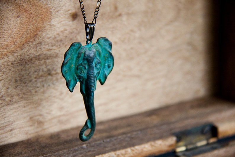 May include: A teal blue elephant pendant necklace with a black chain. The elephant is detailed with a textured surface and a curled trunk.