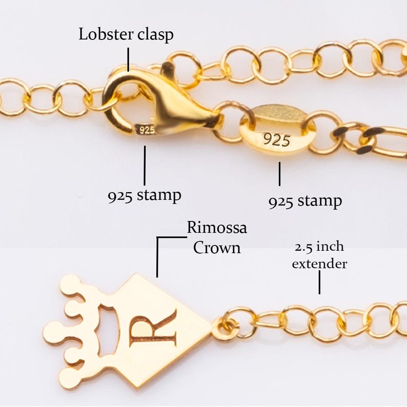 May include: Close-up of a gold-colored necklace with a lobster clasp and a 2.5-inch extender. The necklace features a crown-shaped pendant with the letter "R" and a "925" stamp. The chain is made of small, connected circles.