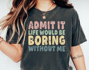 May include: Dark gray t-shirt with the text "ADMIT IT LIFE WOULD BE BORING WITHOUT ME" in pastel colors. The shirt is worn with blue jeans and white sneakers. The overall theme is casual wear.