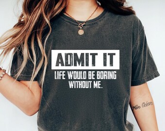 May include: Dark gray t-shirt with the text "ADMIT IT LIFE WOULD BE BORING WITHOUT ME" in a white rectangular box. The shirt is paired with blue jeans and white sneakers. A necklace and bracelet are also visible.