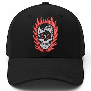 Op de afbeelding: Zwarte baseballcap met een geborduurd ontwerp van een schedel omringd door vlammen. De schedel heeft rode ogen en de vlammen zijn rood en oranje. De cap heeft een gebogen klep en een knoop aan de bovenkant.