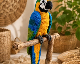 May include: A crocheted macaw parrot figurine featuring vibrant blue, yellow, and green yarn. The bird has a black beak, white facial patches, and dark gray feet, perched on a horizontal wooden stand with wrapped rope accents at the joints.