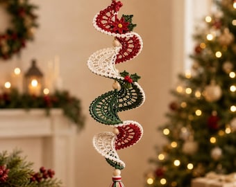May include: A spiral-shaped hanging ornament crafted from crocheted yarn in red, white, and dark green. The design features small wooden beads, a red poinsettia flower, green holly leaves, and a multi-colored tassel at the bottom end.