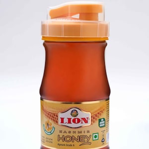 May include: A bottle of Lion Kashmir Honey with a clear, amber-colored liquid. The bottle has an orange lid and a label with the brand name and "Kashmir Honey" in bold letters. The label also indicates "No Added Sugar".
