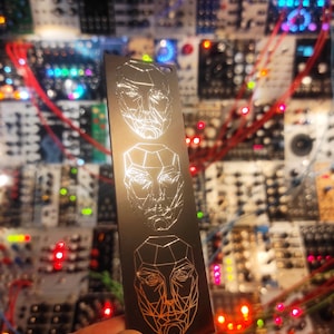 May include: A silver metal keychain with three different geometric face designs engraved on it. The faces are in a vertical line, with the top face being the most detailed and the bottom face being the least detailed.