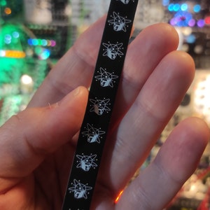 May include: A black metal strip with a repeating pattern of white atom symbols. Each atom symbol has a small square inside, representing a nucleus.