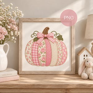 May include: A framed square wall art piece featuring an embroidered pumpkin design. The pumpkin is composed of vertical panels with various pink and white patterns, including floral prints, gingham, polka dots, and cable knit, topped with a bow.