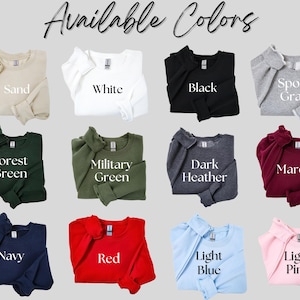 Op de afbeelding: Een selectie van crewneck sweatshirts in verschillende kleuren, waaronder zand, wit, zwart, sportgrijs, bosgroen, legergroen, donkergrijs, bordeauxrood, marineblauw, rood, lichtblauw en lichtroze. De tekst "Available Colors" staat bovenaan.