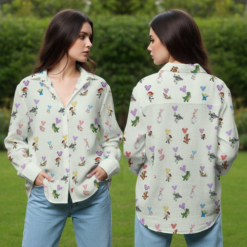 May include: A button-down shirt with a light background, covered in colorful cartoon character and heart-shaped balloon patterns. The long-sleeved shirt is paired with blue jeans. The shirt's design includes characters like Mickey Mouse and dinosaurs.