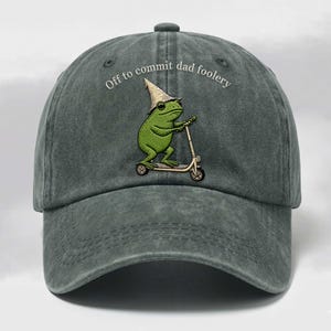 Könnte beinhalten: Graue Baseballkappe mit dem Text "Off to commit dad foolery". Die Kappe zeigt ein gesticktes Bild eines grünen Frosches auf einem Roller. Der Frosch trägt einen kegelförmigen Hut.