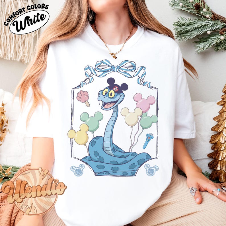 Puede incluir: Camiseta blanca con una serpiente de dibujos animados con orejas de Mickey Mouse y globos. La serpiente es azul claro y sonr&iacute;e. La camiseta tiene las palabras "Comfort Colors White" en un dise&ntilde;o circular.