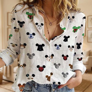 May include: White button-down shirt featuring a repeating pattern of Mickey Mouse-shaped character designs from Star Wars. The characters include Darth Vader, Boba Fett, and Stormtroopers. The long-sleeved shirt is made of a lightweight fabric.