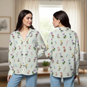 May include: A button-down shirt with a light green background, covered in colorful cartoon character and heart-shaped balloon graphics. The long-sleeved shirt is worn by a person in blue jeans.