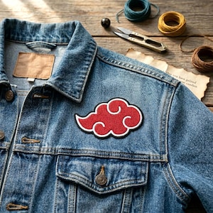 May include: A denim jacket with a red cloud patch. The patch has a white outline and a textured appearance. The jacket has a classic design with button closures and pockets. The background includes sewing supplies.