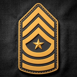 May include: A military rank patch featuring a gold-colored chevron design with three stripes and a central five-pointed star set against a black background. The emblem has a pointed top and rounded bottom edges with visible gold stitching along the border.