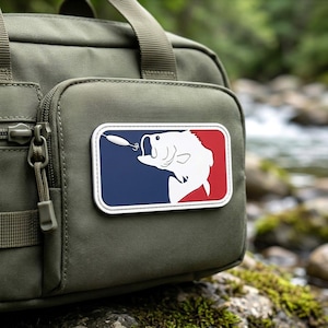 May include: An olive green tactical bag featuring a rectangular patch with a white silhouette of a fish biting a fishing lure. The patch background is divided into a dark blue section on the left and a red section on the right with a white border.