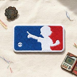 May include: Embroidered patch featuring a white silhouette of a person pointing, set against a blue and red background, with a white border. A small white and blue ball is on the left side. The patch is rectangular and has a stitched design.