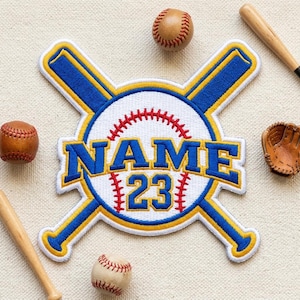 May include: A baseball-themed patch with the word "NAME" and the number "23" in blue and yellow, set against a white baseball design. Two crossed baseball bats, two baseballs, a baseball glove, and two baseball bats are also visible.