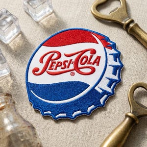 May include: Embroidered patch in the shape of a Pepsi-Cola bottle cap. The patch features the Pepsi-Cola logo in red script on a white background, with a red and blue color scheme. Two vintage bottle openers are visible.