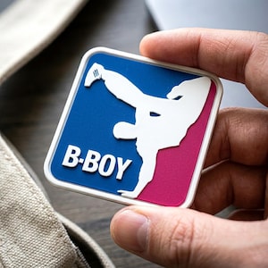 May include: A square-shaped patch with rounded corners featuring a blue and magenta background. A white silhouette of a person performing a breakdancing move is centered on the patch, with the white text B-BOY printed in the lower left corner.