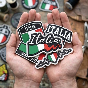May include: A collection of rubberized patches featuring the Italian flag colors of green, white, and red. The patches display the text Italia in various fonts and styles, including one with a heart shape and an EKG heartbeat line graphic.