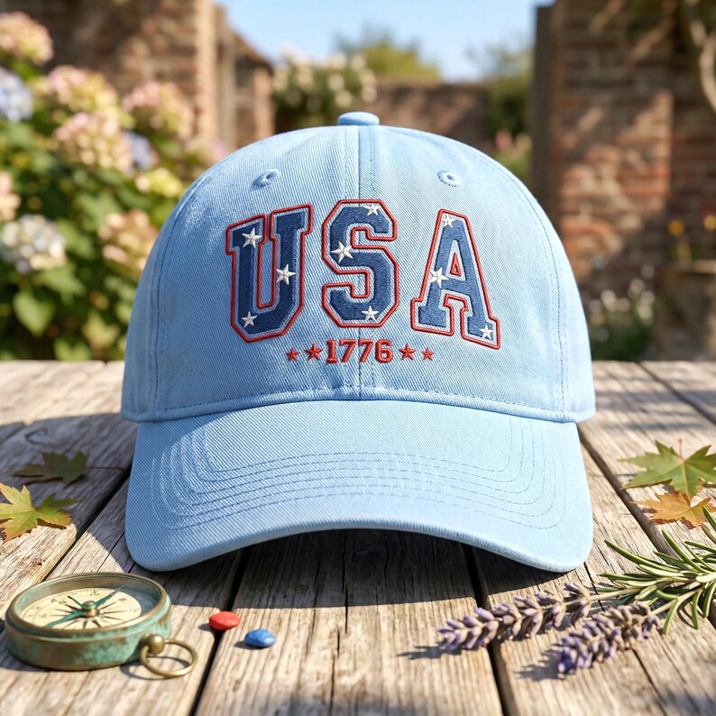 May include: A light blue baseball cap with the word "USA" embroidered in red and white, along with the year "1776". The cap is made of a soft material and has a curved brim. The cap is sitting on a wooden surface.