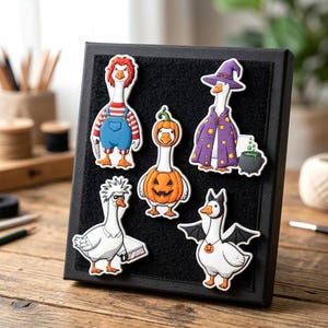 May include: A black display board featuring five goose-shaped magnets dressed in Halloween costumes: a doll-like figure, a pumpkin, a purple-robed wizard with a cauldron, a character with spiky hair holding a saw, and a bat-winged goose.