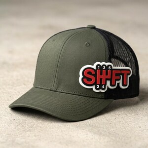 May include: An olive green baseball cap with a black mesh back and a structured crown. A white, black, and red rubberized patch on the front displays the text SHFT with a manual transmission gear shift pattern featuring numbers 1, 2, 3, 4, and 5.