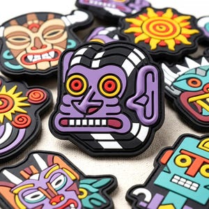 May include: A collection of colorful rubberized patches featuring various stylized character faces and sun motifs. The central patch displays a purple face with large yellow and red eyes, a prominent ear, and white teeth, all outlined in black rubber.