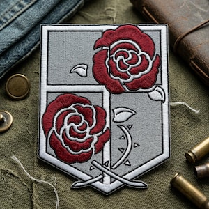 May include: Embroidered patch featuring a gray shield design with two red roses and white accents. The patch has a white border and includes a stem with thorns and crossed swords. The patch is likely for clothing or accessories.