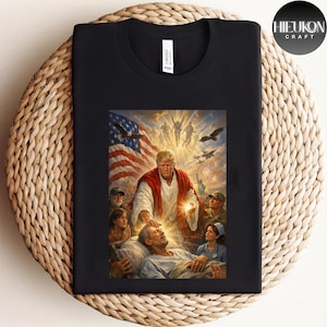 Può includere: T-shirt nero con una vivace stampa grafica. Il design mostra una scena religiosa con una bandiera americana, figure e testo. La maglietta è realizzata in materiale morbido e ha un girocollo.