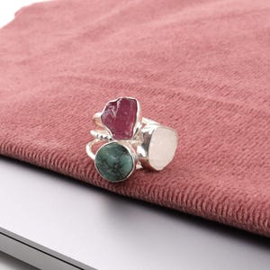 May include: A collection of silver rings, each featuring a unique gemstone. The rings showcase a variety of colors, including a deep red, a pale pink, and a vibrant green. The gemstones are set in a polished silver band.