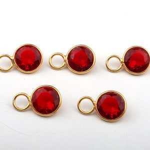 May include: Five circular charms featuring faceted red crystals set in gold-toned metal bezels. Each charm includes a small, round jump ring attached to the side, designed for jewellery making or decorative attachment to various craft projects.