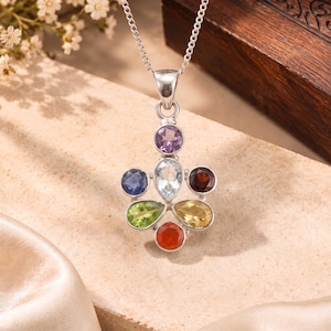 Può includere: Una collana con pendente in argento caratterizzata da sette pietre preziose multicolori disposte a grappolo. Le pietre includono un'ametista rotonda viola, un topazio azzurro a forma di pera, uno zaffiro rotondo blu scuro, un granato rotondo rosso scuro, un peridoto verde a forma di pera, un citrino giallo a forma di pera e una corniola rotonda arancione.