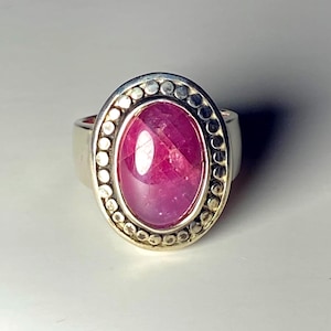 May include: A silver ring featuring a large, oval-shaped, vibrant pink gemstone. The gemstone is surrounded by a border of small, evenly spaced silver beads. The ring's band is a simple, polished silver.