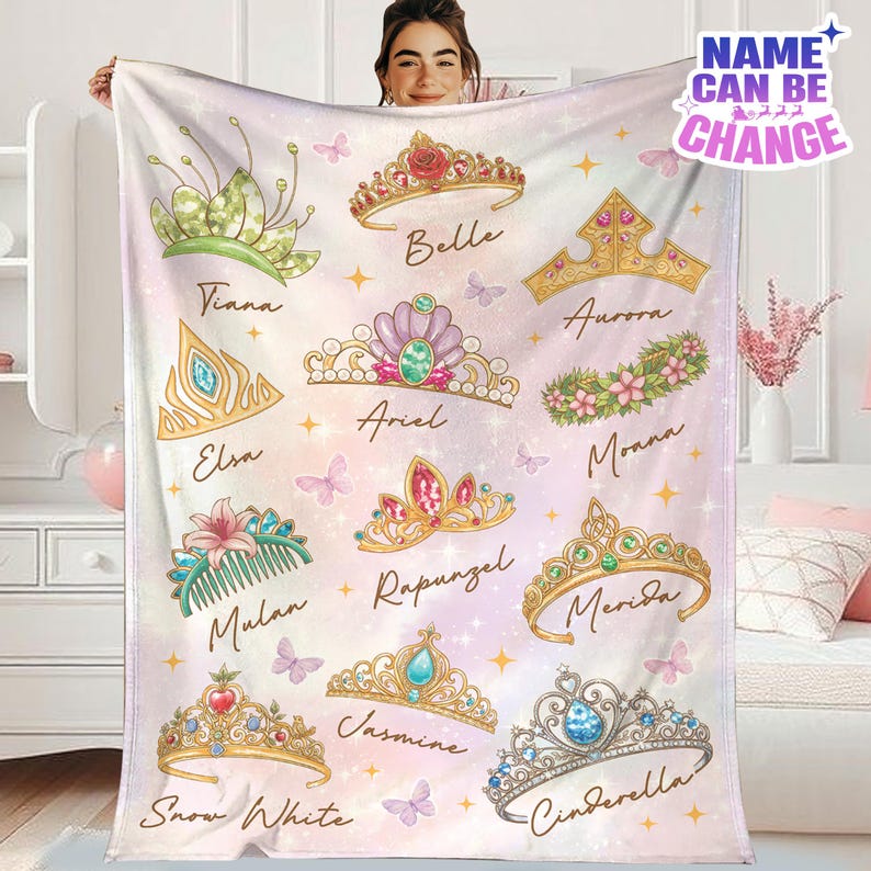 A person is holding up a blanket with various Disney princess crowns and names printed on it.