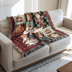 a cozy couch with a colorful, patterned blanket or throw on it. The blanket has a variety of designs and colors, including a Christmas-themed design with a snowman, gingerbread man, and other festive elements. The blanket is placed on a white couch, and there is a wooden coffee table in the foreground.