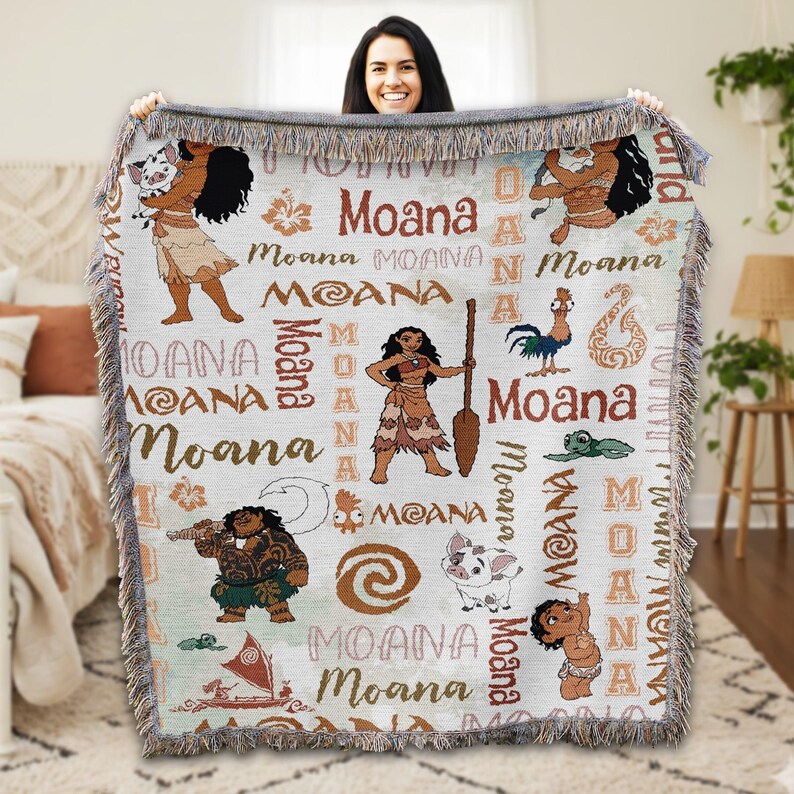A woman is holding up a colorful blanket with the Moana characters from the Disney animated film Moana.