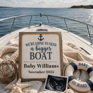 Könnte beinhalten: Ein rechteckiges Holzschild mit Seilrand, einem dunkelblauen Anker-Symbol und dem Text WE'RE GOING TO NEED a bigger BOAT, Baby Williams und November 2025. Dazu eine Glasflasche, ein Seestern und ein Rettungsring mit der Aufschrift BABY ON BOARD.