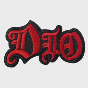 May include: Embroidered patch featuring the word "DIO" in a bold, gothic font. The letters are red with a black border, creating a striking contrast. The patch is likely designed for application on clothing or accessories.
