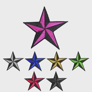 Op de afbeelding: Geborduurde sterpatches in diverse kleuren, waaronder zwart, grijs, blauw, geel, groen, rood en roze met zwart. De patches zijn stervormig en geschikt voor kleding of accessoires.