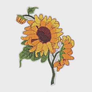 Könnte beinhalten: Gestickter Sonnenblumen-Aufnäher mit einer großen, offenen Blüte, gelben Blütenblättern und einem dunkelbraunen Zentrum. Der Aufnäher enthält eine kleinere Knospe und eine zweite, teilweise geöffnete Blüte, alle mit grünen Blättern und Stielen. Zum Aufnähen oder Aufbügeln.
