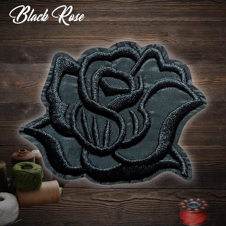 Puede incluir: Parche de rosa negra bordada con el texto "Black Rose" en cursiva. El parche es negro con costuras detalladas, sobre un fondo de madera. La rosa es el punto focal.