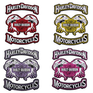 May include: Four embroidered Harley-Davidson patches featuring a central eagle head design flanked by text banners. The sets are color-coded in red, yellow, purple, and pink, each displaying the Harley-Davidson Motor Cycles logo and brand name.