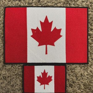 May include: Two rectangular patches featuring the Canadian flag. The flag design includes a red maple leaf centered on a white square, flanked by red vertical bars. The patches are in different sizes, with a black border.