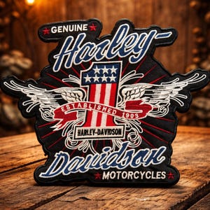 May include: A black embroidered patch featuring the text Genuine Harley-Davidson Motorcycles. The design includes a large number one with red and white stripes, white stars, and white wings. A red banner reads Established 1903.
