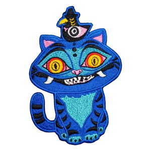 May include: Embroidered patch featuring a blue cat with a whimsical design. The cat has large yellow eyes, a toothy grin, and a small bird wearing a hat on its head. The patch has a detailed, stitched appearance.