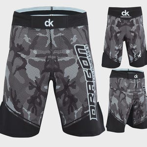 May include: Black and gray camouflage fight shorts with the text "DRAGON FIGHTWEAR" in white. The shorts have a black waistband with the letters "ck" and a light blue trim. Additional shorts are displayed in the image.