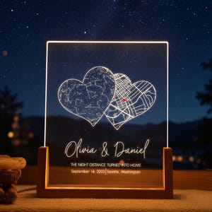 May include: A rectangular acrylic light panel in a wooden base featuring two heart-shaped designs, one with a star map and one with a street map. The text reads Olivia & Daniel, The night distance turned into home, September 14, 2023, Seattle, Washington.
